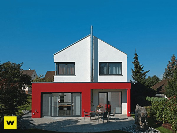 Modernes Einfamilienhaus mit Flachdach und roter Fassade im grünen Garten bei Sonnenschein.