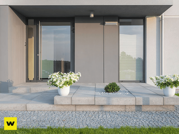 Moderner Hauseingang mit großen Glasfronten, Pflanzkübeln und gepflastertem Weg.